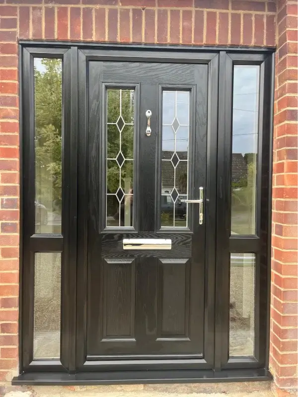 Black composite front door with decorative glazing and full-height side windows in a brick entrance. Installed by Norfolk Exterior Solutions.